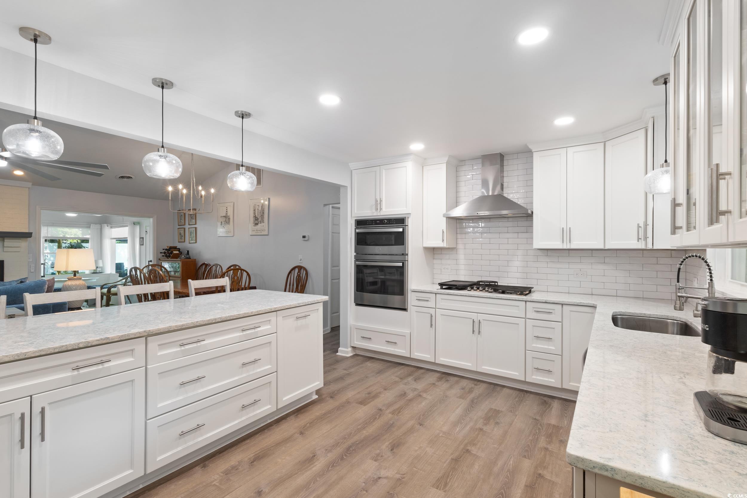 815 Tillson Road North Myrtle Beach, SC 29582 - Photo 4 of 39 Kitchen with light wood-type flooring, wall chimney range hood, ceiling fan, tasteful backsplash, and white cabinets