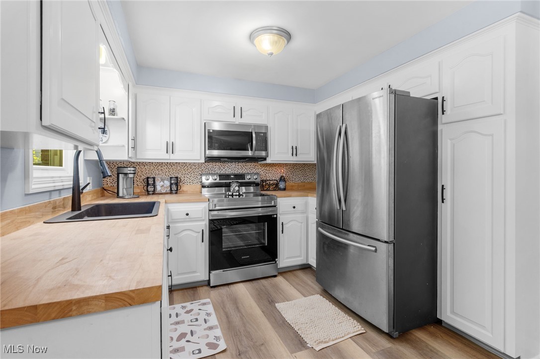 4895 3rd Street Northwest Canton, OH 44708 - Photo 10 of 27 Kitchen featuring appliances with stainless steel finishes, white cabinets, backsplash, and light wood-style floors