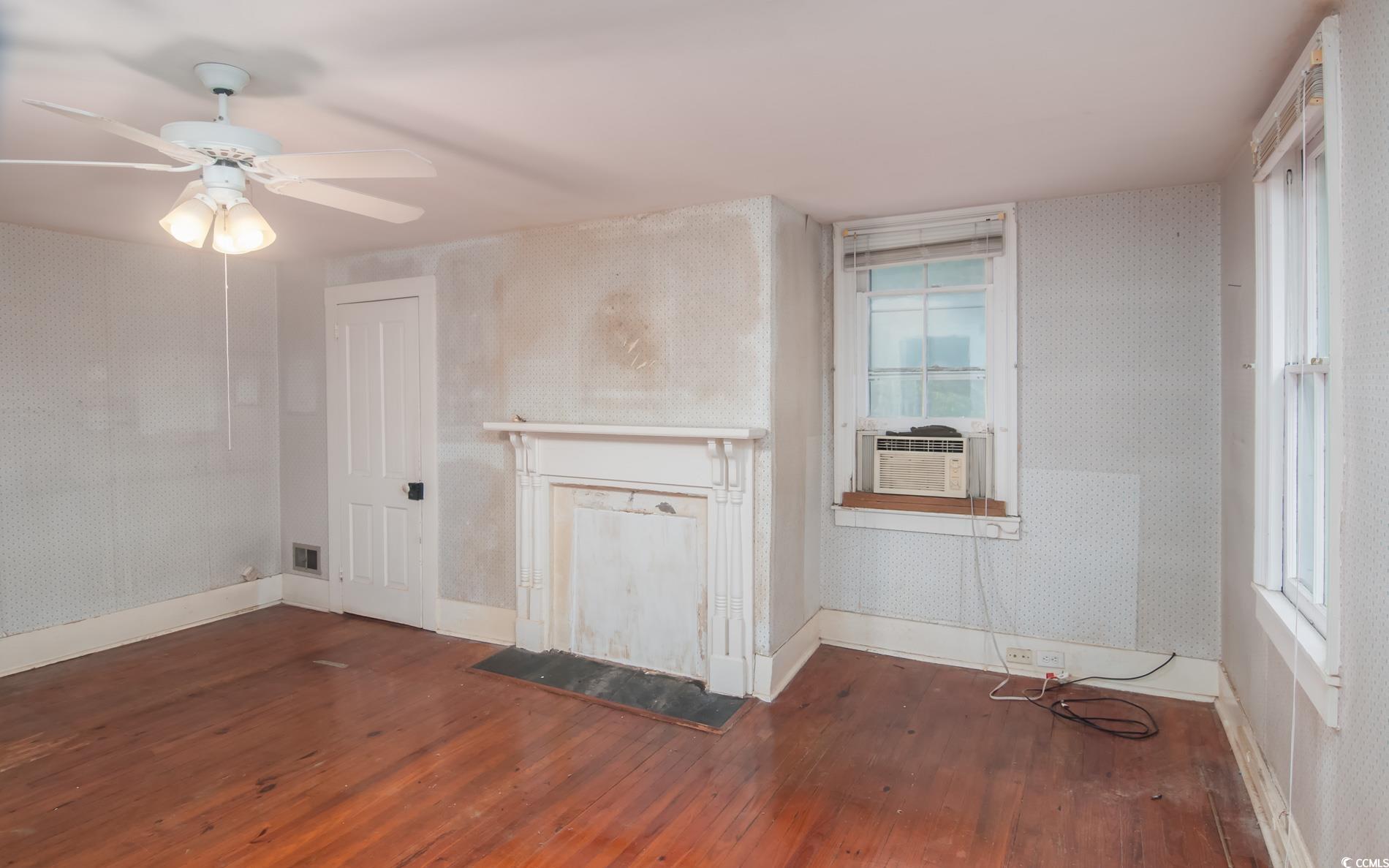 1010 Highmarket Street Georgetown, SC 29440 - Photo 22 of 32 Unfurnished living room featuring dark wood-style flooring, wallpapered walls, a ceiling fan, cooling unit, and a fireplace with flush hearth