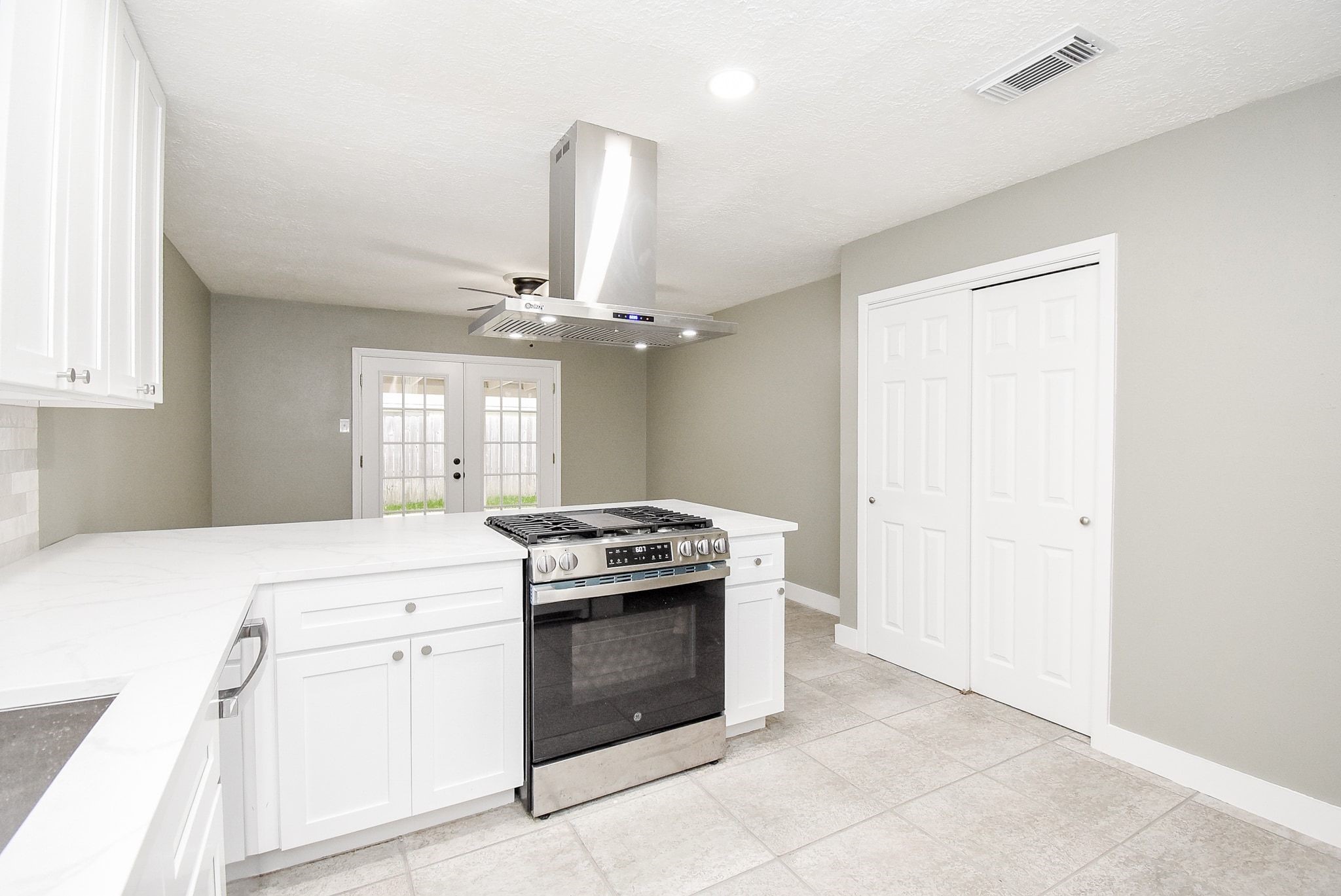 17330 Modbury Drive Spring, TX 77379 - Photo 11 of 30 Modern kitchen featuring sleek white cabinetry, a central island with a built-in stove, and elegant tile flooring leading to double French doors.