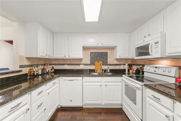 a kitchen with granite countertop white cabinets white stainless steel appliances a sink and dishwasher with wooden floor