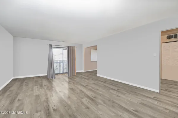 a view of an empty room with wooden floor and windows