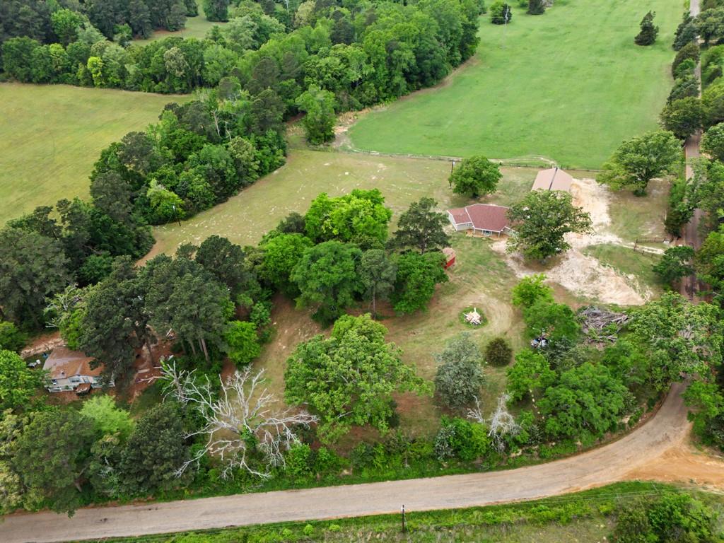 1129 Holly Road Gilmer, TX 75644 - Photo 27 of 31 Expansive property featuring a single-story residence with a red-shingled roof, surrounded by mature trees and open green pastures
