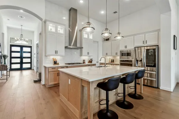 a kitchen with stainless steel appliances kitchen island granite countertop a stove a sink a refrigerator and chairs with wooden floor
