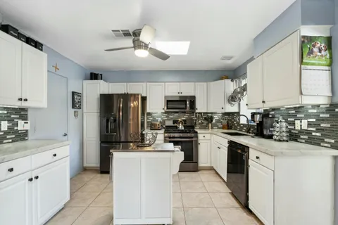 a kitchen with stainless steel appliances granite countertop a stove a sink dishwasher and white cabinets with wooden floor