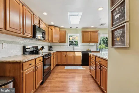 a kitchen with stainless steel appliances granite countertop wooden cabinets a sink and dishwasher a stove top oven with wooden floor