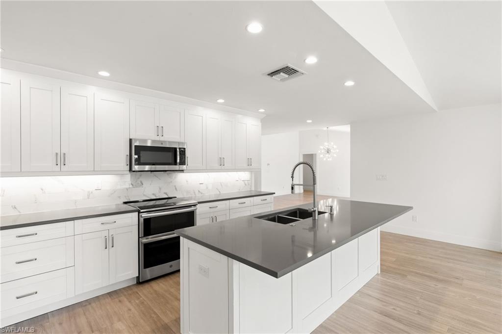 2178 Pinewoods Circle, Unit 25 Naples, FL 34105 - Photo 12 of 45 a kitchen with stainless steel appliances granite countertop a sink a stove and white cabinets with wooden floor