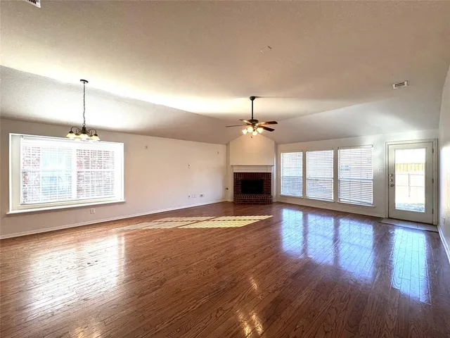 a view of an empty room with wooden floor fireplace and a window
