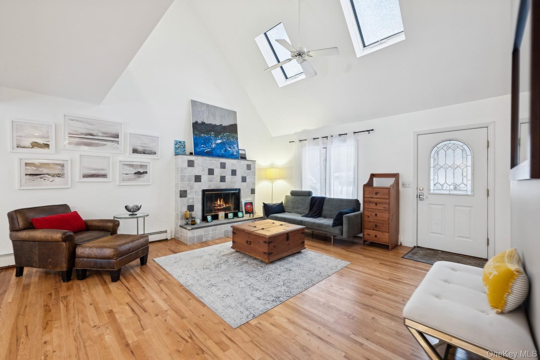 12 Hildreth Road Hampton Bays, NY 11946 - Photo 5 of 21 Living room with a healthy amount of sunlight, a tiled fireplace, high vaulted ceiling, and a skylight