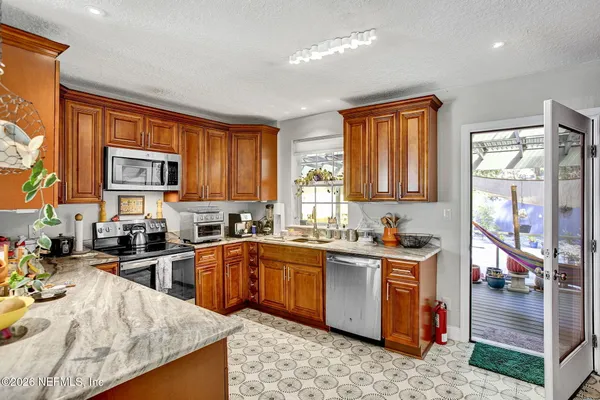 a kitchen with stainless steel appliances granite countertop wooden cabinets a sink dishwasher a stove and a refrigerator with wooden floor