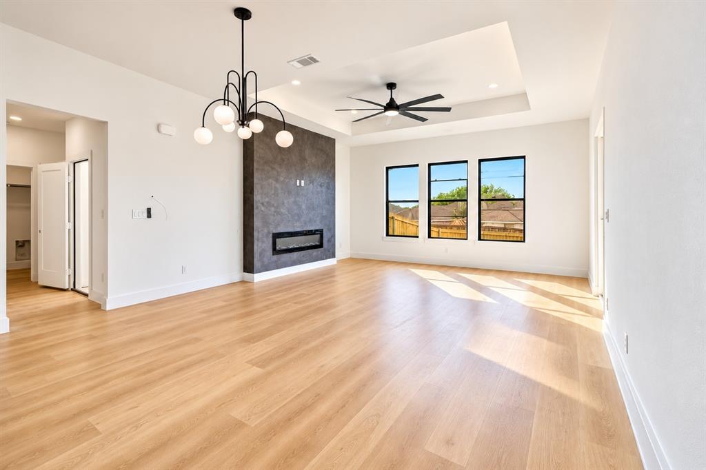 1640 West Wintergreen Road Lancaster, TX 75134 - Photo 9 of 37 Expansive living area featuring wood-finish flooring, a contemporary chandelier, a ceiling fan, an electric fireplace with a textured surround, and three large windows
