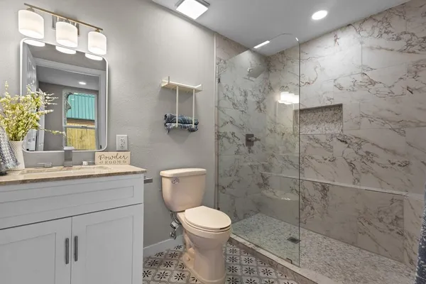 a bathroom with a toilet sink vanity granite and shower