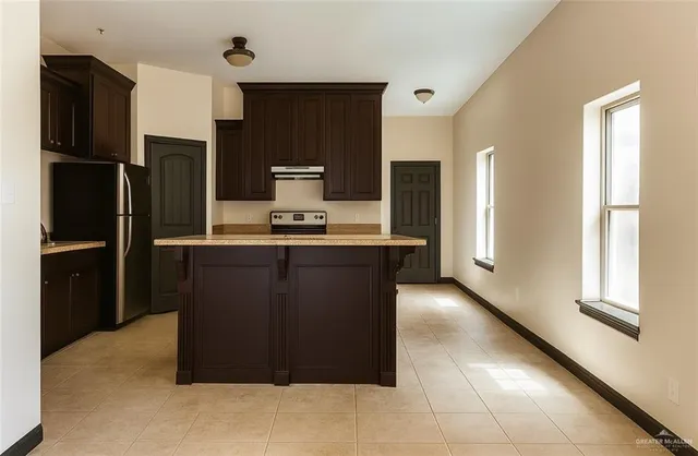 a kitchen with kitchen island stainless steel appliances a refrigerator counter space and a window