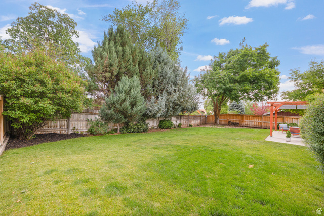 3320 Cherokee Lane Provo, UT 84604 - Photo 47 of 52 Expansive backyard featuring a lush green lawn, mature trees, a wood privacy fence, and a concrete patio with a wooden pergola