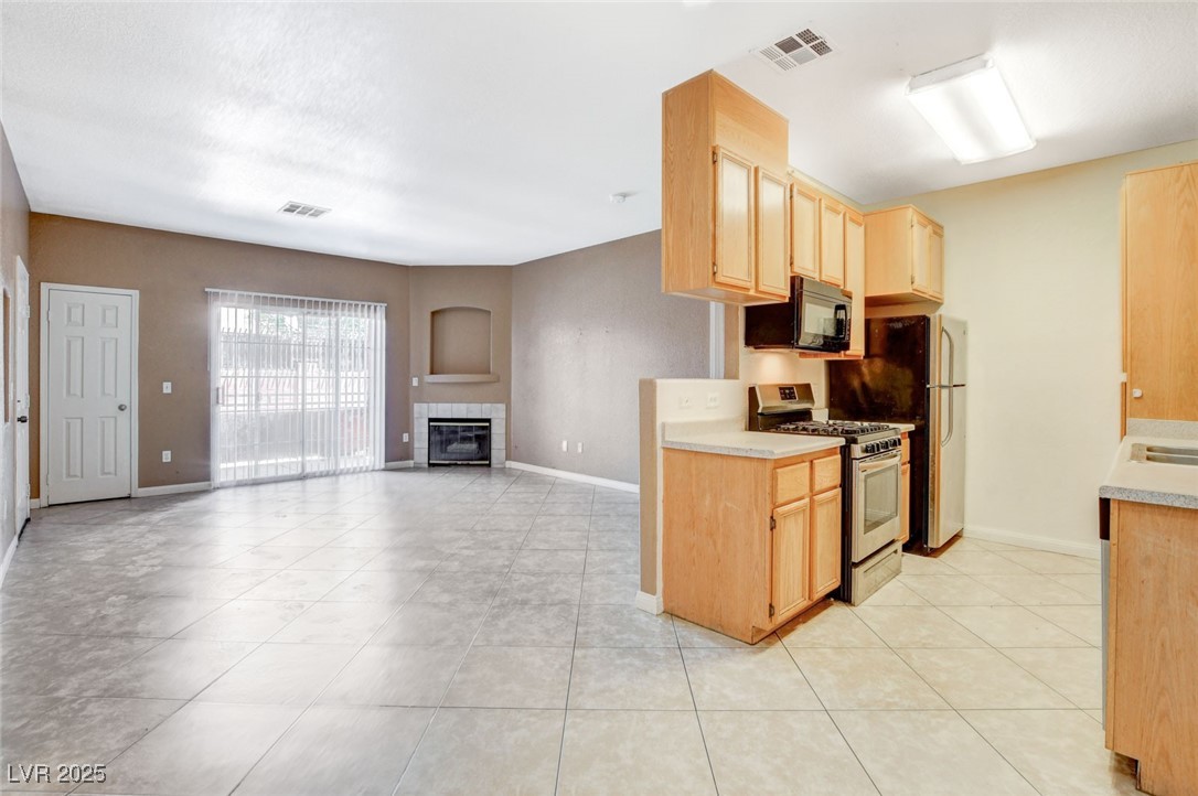 4730 East Craig Road, Unit 1005 Las Vegas, NV 89115 - Photo 12 of 45 Kitchen with stainless steel gas stove, black microwave, a fireplace, light countertops, and light brown cabinetry