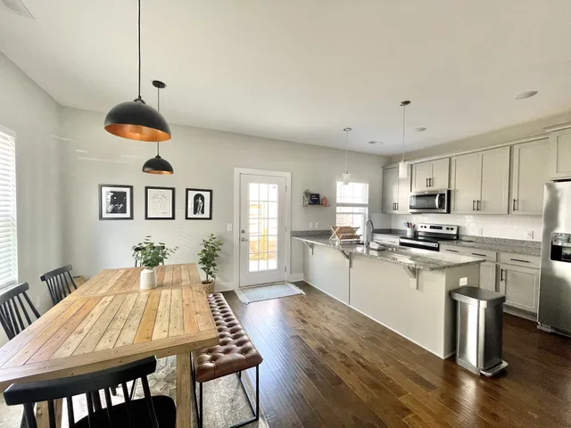 a kitchen with stainless steel appliances granite countertop a stove a sink dishwasher a dining table and chairs with wooden floor