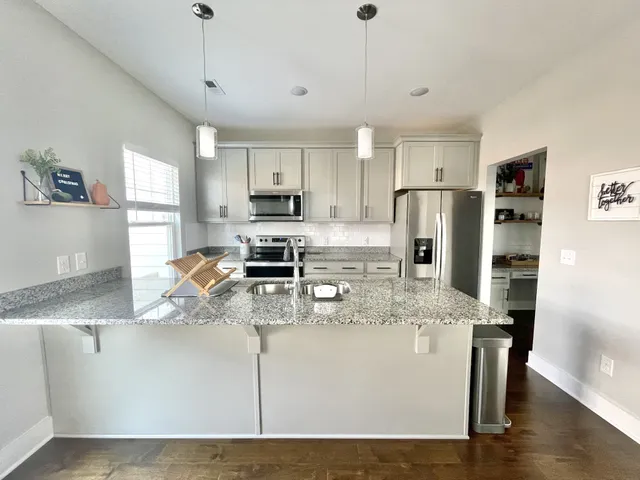 a kitchen with stainless steel appliances granite countertop a refrigerator a stove a sink dishwasher a oven with white cabinets and wooden floor