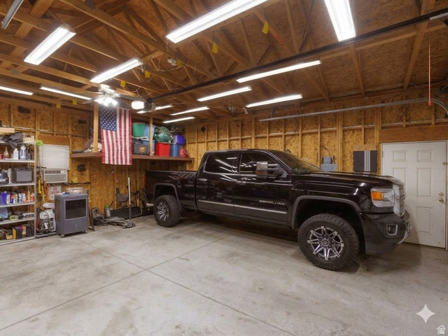 8252 Wood Street Midvale, UT 84047 - Photo 31 of 40 Spacious garage featuring exposed wood beam ceiling, multiple fluorescent light fixtures, large concrete flooring, and built-in shelving