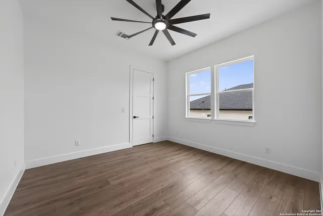 an empty room with wooden floor chandelier fan and windows