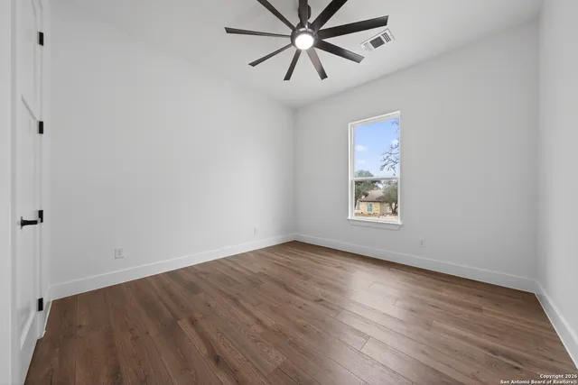 an empty room with wooden floor chandelier fan and windows