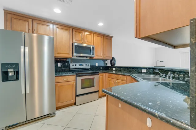 a kitchen with stainless steel appliances granite countertop a refrigerator a stove and a sink with wooden cabinets