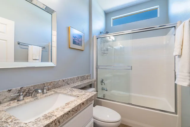 a bathroom with a granite countertop bathtub shower sink vanity and toilet