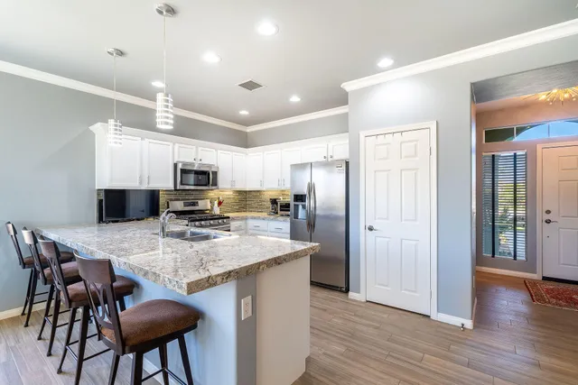 a kitchen with stainless steel appliances kitchen island granite countertop a table chairs refrigerator and microwave