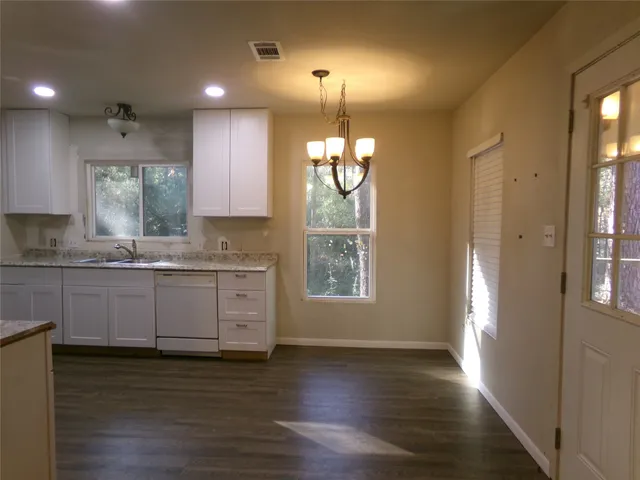 a kitchen with granite countertop wooden floors white cabinets and window