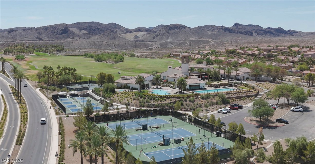3 Rue Promenade Way Henderson, NV 89011 - Photo 13 of 26 An aerial panorama reveals a vast community complete with multiple sports courts, a sparkling pool, and a sprawling golf course, all set against a dramatic mountainous backdrop.