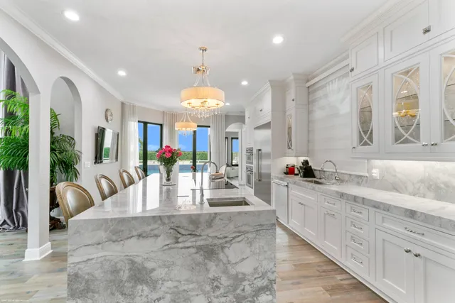 a large kitchen with granite countertop a large counter top a sink stainless steel appliances and chandelier