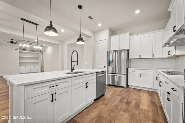 a kitchen with stainless steel appliances kitchen island granite countertop a refrigerator a sink dishwasher a stove and white cabinets with wooden floor