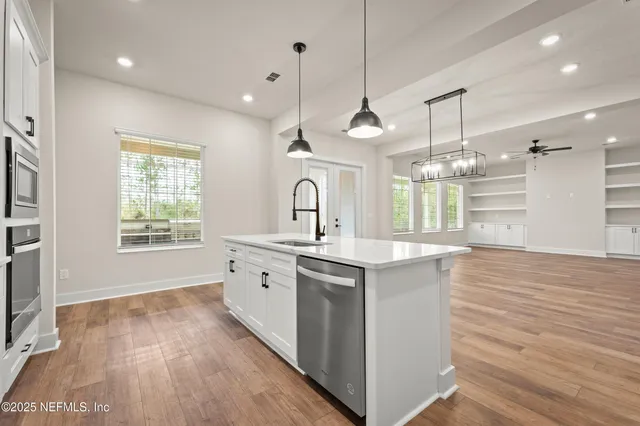 a large kitchen with stainless steel appliances a large counter top a sink a window and wooden floor
