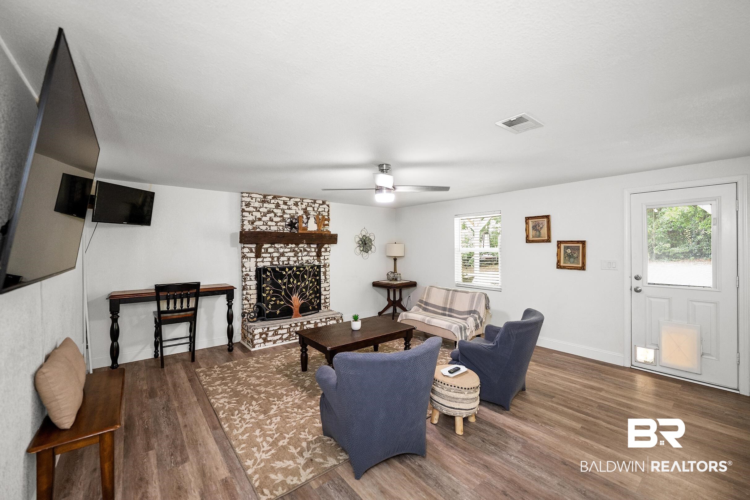 33129 Antietam Road Lillian, AL 36549 - Photo 4 of 31 Spacious living area featuring wood-finish flooring, a white brick fireplace with a wood mantel, and multiple windows providing natural light