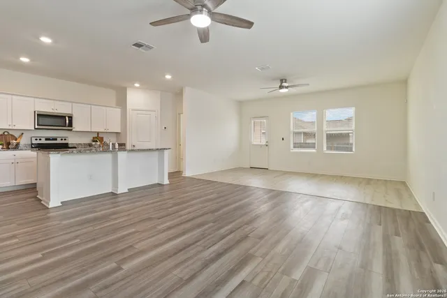 an empty room with wooden floor a ceiling fan and kitchen view