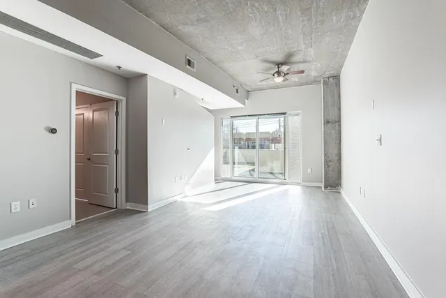 an empty room with wooden floor fan and windows