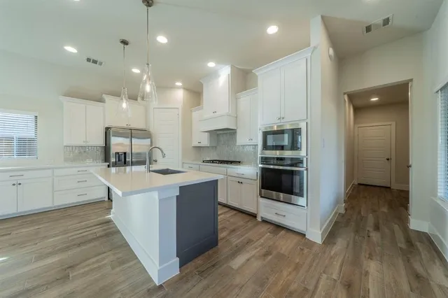a view of an empty room with wooden floor and a kitchen
