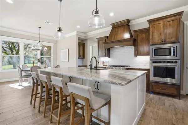 a kitchen with stainless steel appliances granite countertop a stove top oven a sink a dining table and chairs with wooden floor