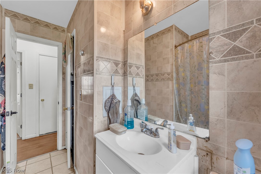 30015 Warren Road Wickliffe, OH 44092 - Photo 11 of 20 Bathroom featuring full wall tile surround, integrated vanity sink, and a large wall-mounted mirror