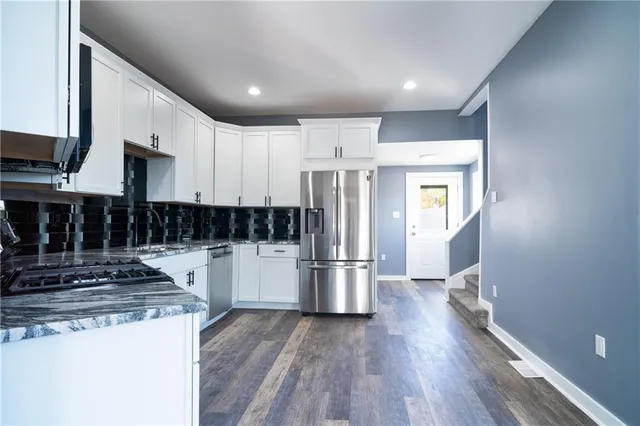 a kitchen with stainless steel appliances granite countertop a refrigerator a stove a sink and white cabinets with wooden floor