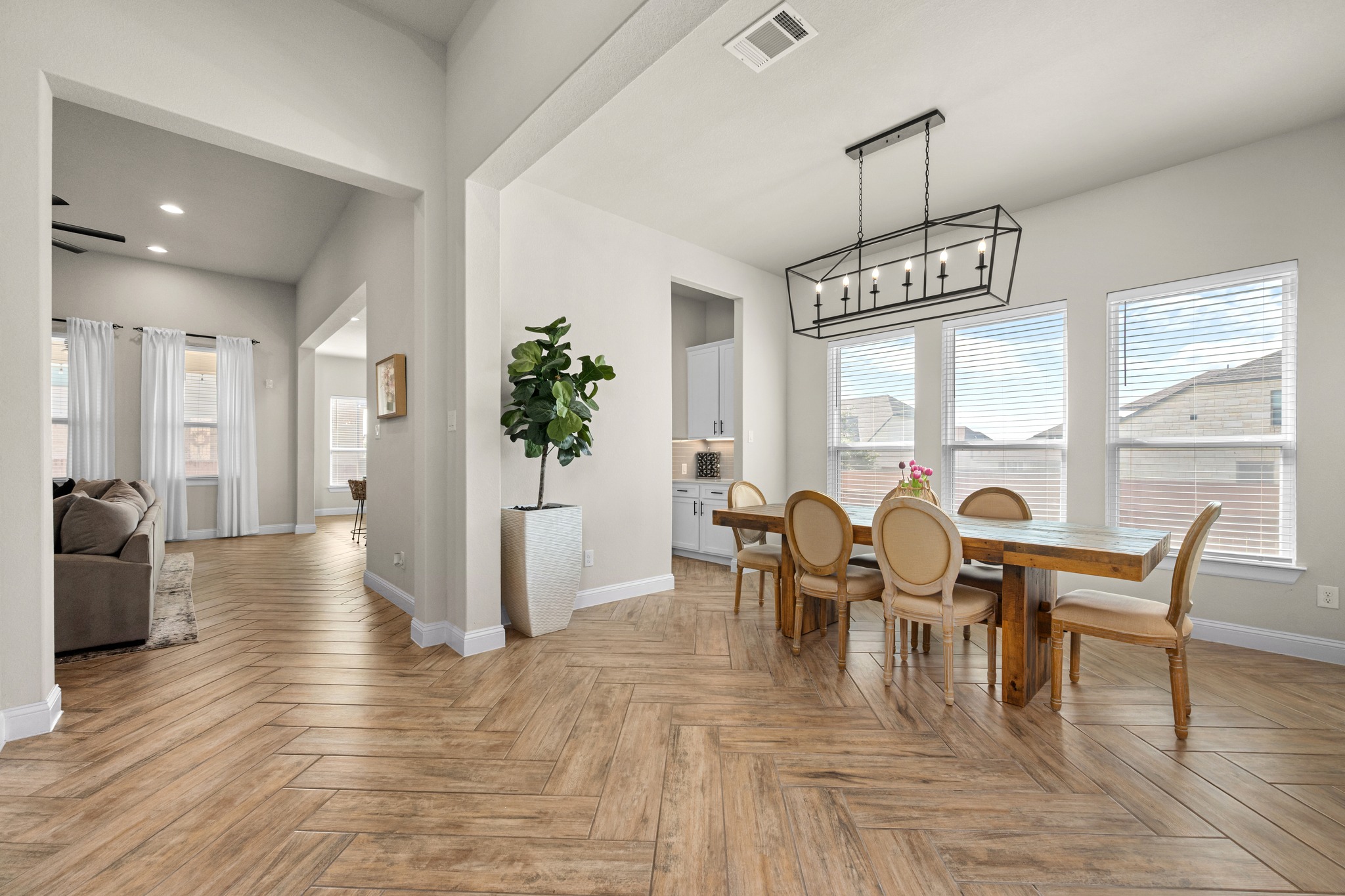 2100 Highland Ridge Road Georgetown, TX 78628 - Photo 5 of 30 Herringbone-patterned floors lead to a sunlit dining area with an open-concept kitchen beyond.
