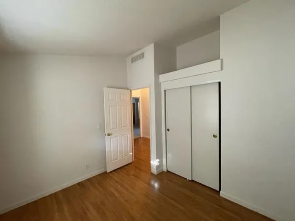 a view of an empty room with wooden floor and closet
