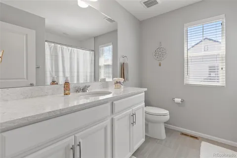 a bathroom with a granite countertop toilet a sink a mirror and a window