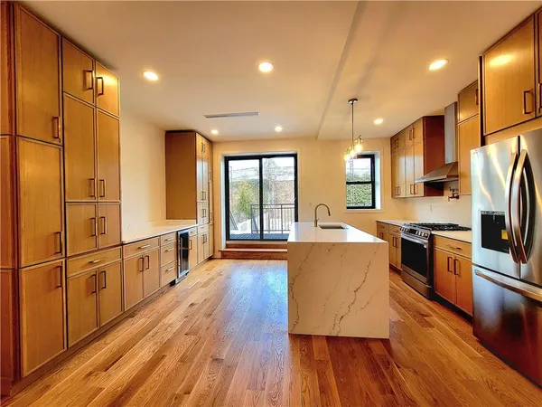 a large kitchen with stainless steel appliances a large counter top a stove a refrigerator cabinets and wooden floor