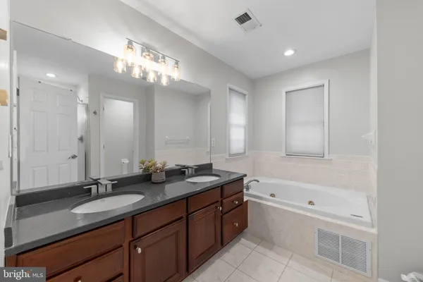 a bathroom with a granite countertop double vanity sink a mirror and a bathtub