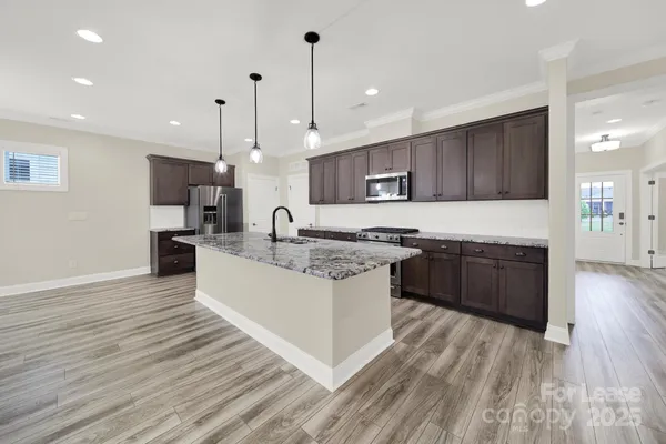 a large kitchen with stainless steel appliances granite countertop a stove a sink dishwasher a refrigerator and a oven with wooden floor