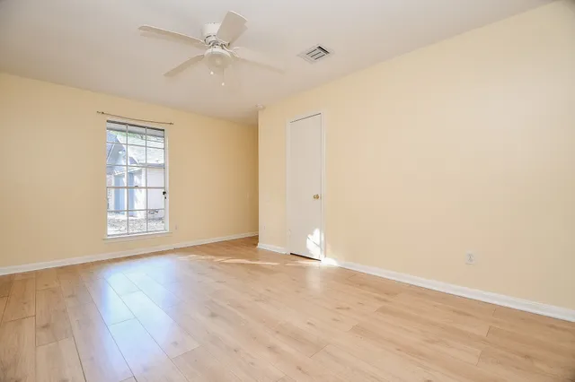 an empty room with wooden floor ceiling fan and windows