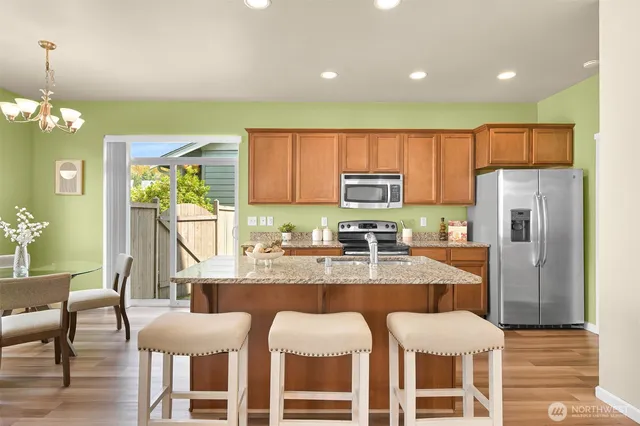 a kitchen with stainless steel appliances granite countertop a dining table chairs refrigerator and microwave