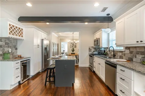 a kitchen with granite countertop a refrigerator a sink dishwasher a stove top oven a dining table and chairs with wooden floor