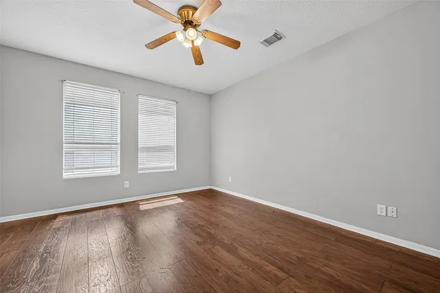 an empty room with wooden floor chandelier fan and windows