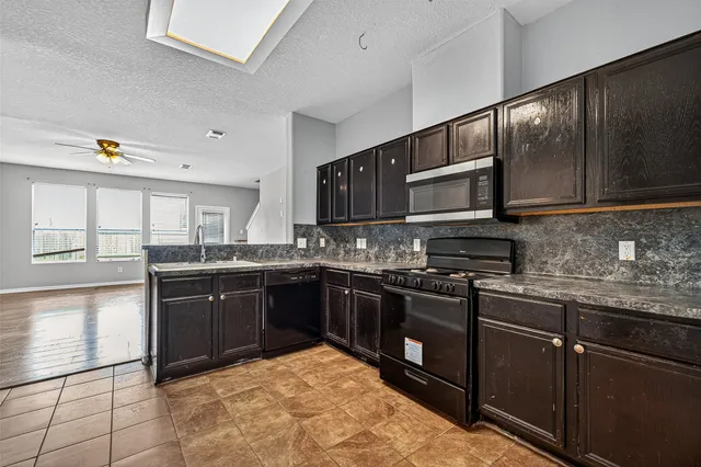 an empty room with kitchen view and a ceiling fan